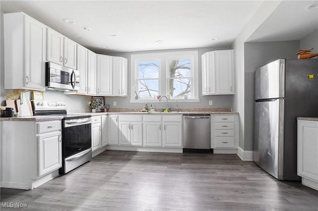 kitchen with appliances with stainless steel finishes, sink, white cabinets, and light hardwood / wood-style floors