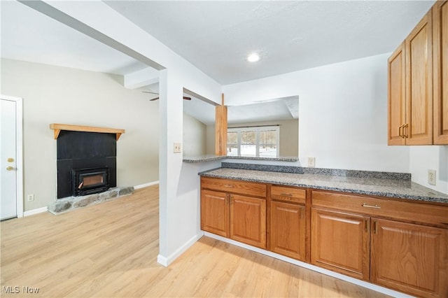 kitchen with lofted ceiling with beams, ceiling fan, light hardwood / wood-style floors, and dark stone countertops