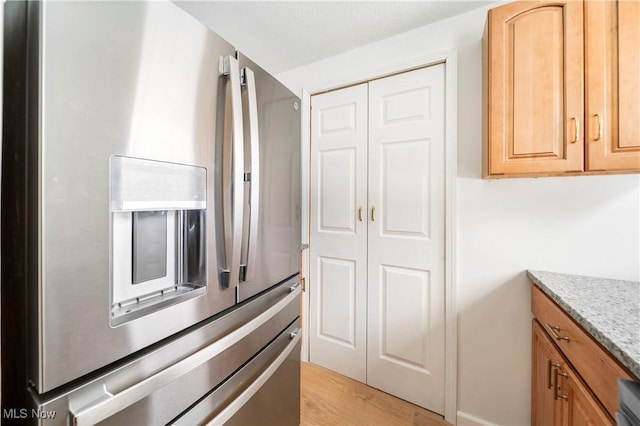 kitchen featuring light brown cabinetry, light stone counters, stainless steel fridge, and light hardwood / wood-style floors