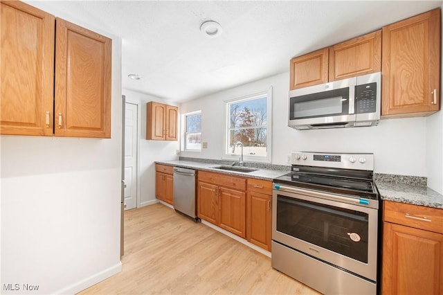 kitchen featuring light stone counters, sink, light hardwood / wood-style floors, and appliances with stainless steel finishes