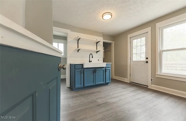 interior space featuring sink, blue cabinetry, a textured ceiling, and light wood-type flooring