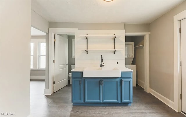 interior space with dark hardwood / wood-style flooring, sink, blue cabinetry, and stacked washer / dryer