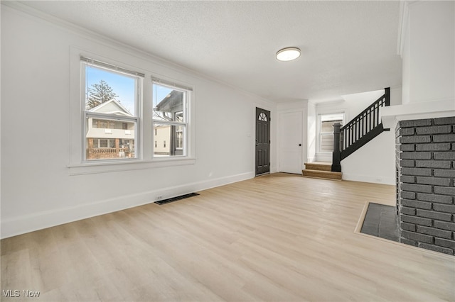 foyer with ornamental molding, a textured ceiling, and light hardwood / wood-style floors