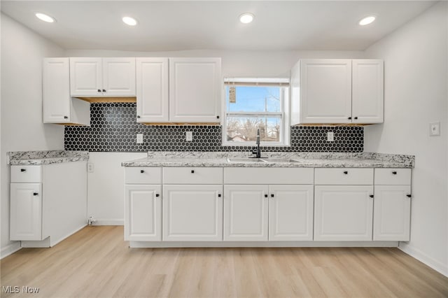 kitchen featuring tasteful backsplash, light wood-type flooring, sink, and white cabinets