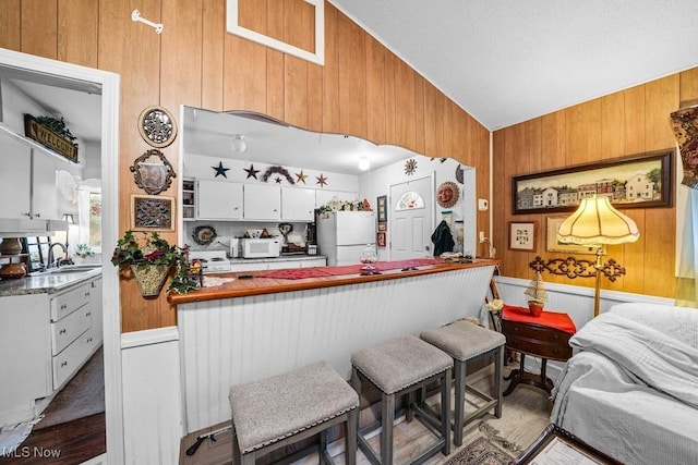 kitchen with lofted ceiling, a breakfast bar, white cabinetry, wooden walls, and white appliances