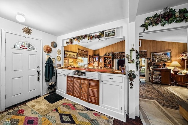 kitchen featuring white cabinetry, wooden walls, and vaulted ceiling