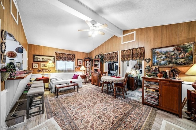 living room with vaulted ceiling with beams, a textured ceiling, wooden walls, and light hardwood / wood-style flooring