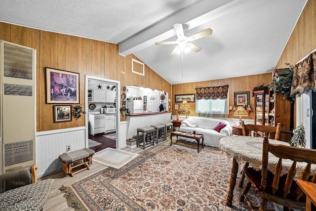 living room with wood walls, wood-type flooring, vaulted ceiling with beams, ceiling fan, and a textured ceiling