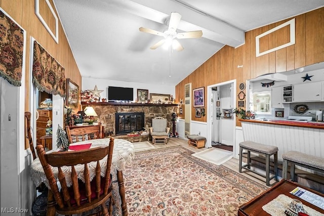 living room featuring wood walls, lofted ceiling with beams, light wood-type flooring, ceiling fan, and a fireplace