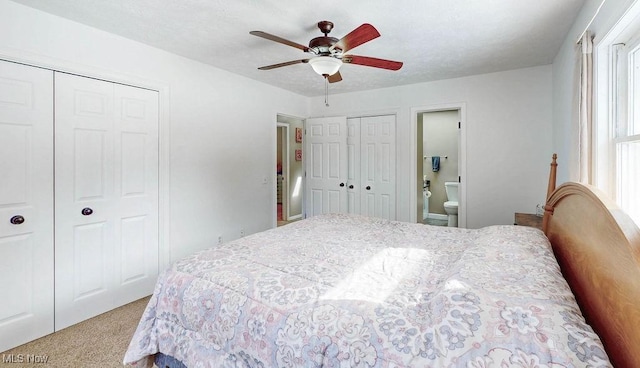 carpeted bedroom featuring multiple closets, ceiling fan, and ensuite bath