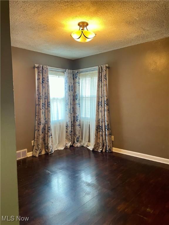 empty room with dark hardwood / wood-style flooring and a textured ceiling