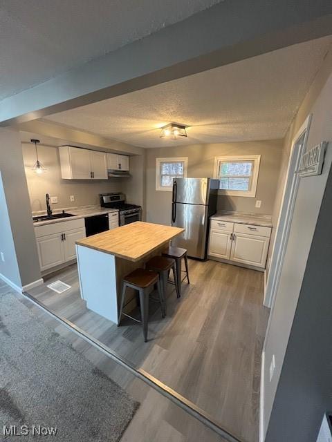 kitchen featuring appliances with stainless steel finishes, white cabinetry, hardwood / wood-style floors, a center island, and a kitchen bar