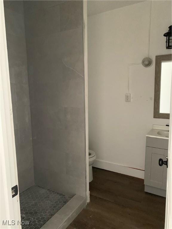 bathroom featuring vanity, wood-type flooring, tiled shower, and toilet