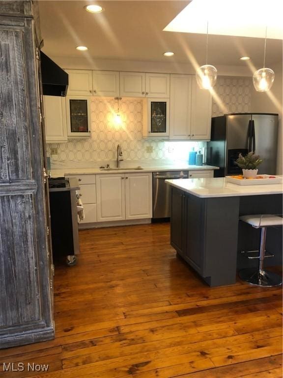 kitchen with appliances with stainless steel finishes, pendant lighting, range hood, sink, and white cabinets