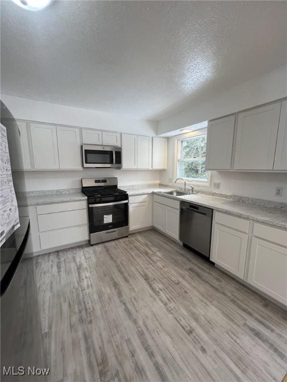 kitchen featuring sink, light hardwood / wood-style floors, white cabinets, and appliances with stainless steel finishes