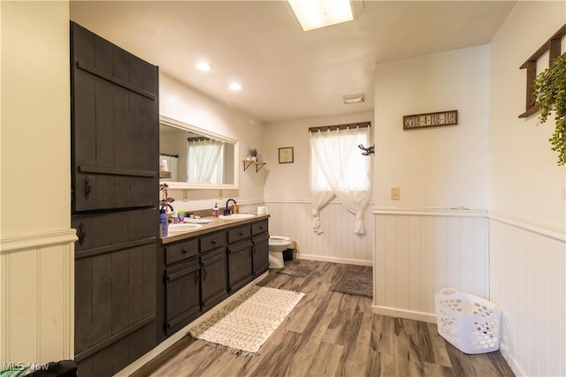 full bath with a wainscoted wall, double vanity, toilet, a sink, and wood finished floors