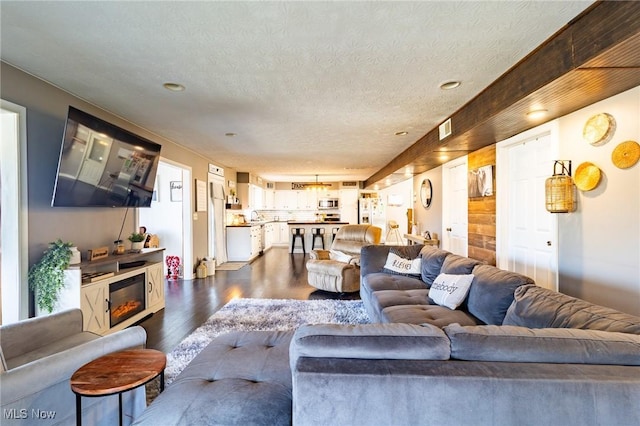 living area featuring a textured ceiling, visible vents, dark wood-type flooring, and a glass covered fireplace