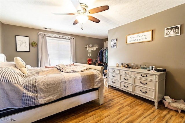 bedroom featuring a ceiling fan, visible vents, a textured ceiling, and light wood finished floors