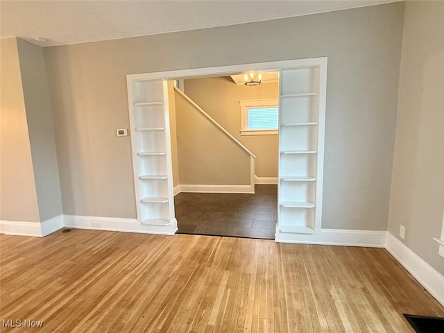 unfurnished room featuring hardwood / wood-style floors, a chandelier, and built in shelves