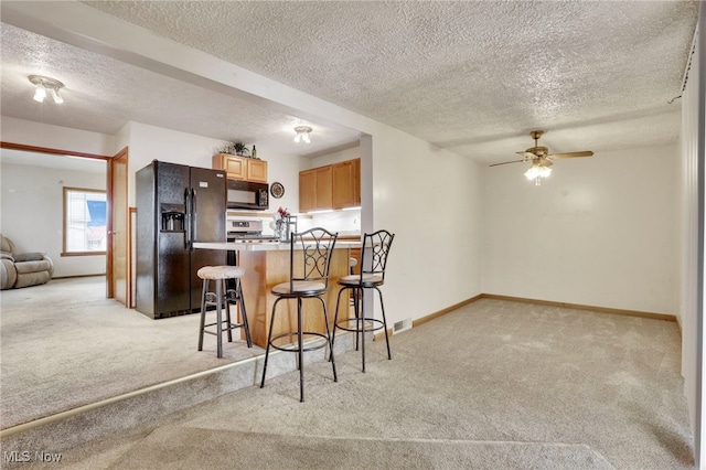 kitchen featuring ceiling fan, light colored carpet, a breakfast bar, and black appliances