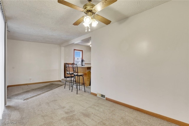 unfurnished room with ceiling fan, light colored carpet, and a textured ceiling