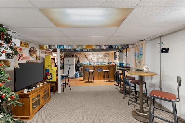 basement with white refrigerator, carpet flooring, bar area, and a drop ceiling