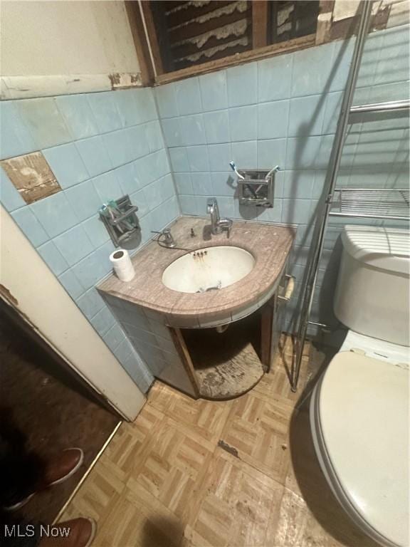 bathroom with parquet floors, toilet, sink, and tile walls