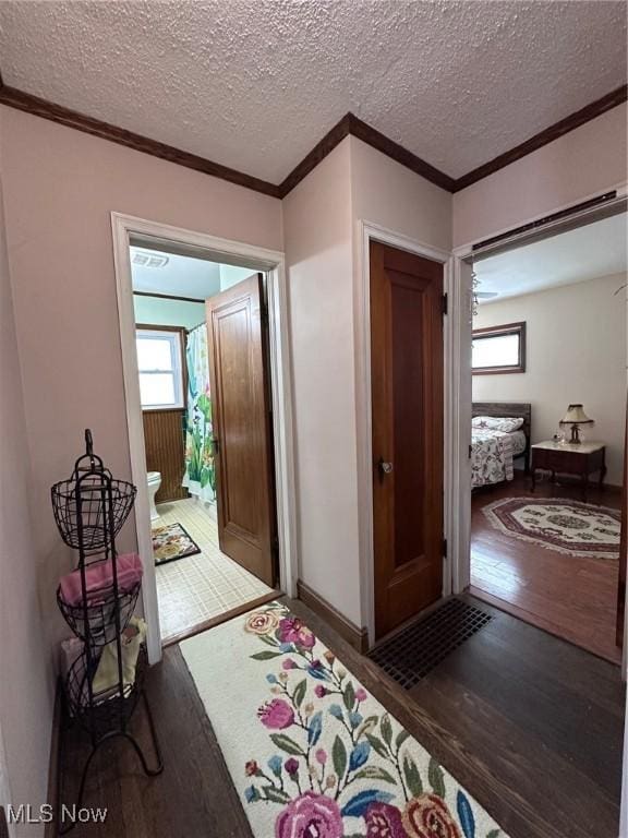 corridor featuring hardwood / wood-style floors, crown molding, and a textured ceiling