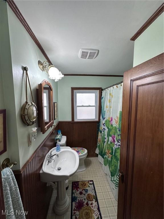 bathroom with crown molding, toilet, and wood walls