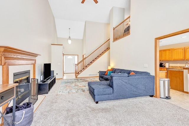 living room with light carpet, visible vents, a ceiling fan, stairs, and a high ceiling