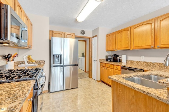 kitchen with light stone counters, washer and clothes dryer, stainless steel appliances, a sink, and a textured ceiling