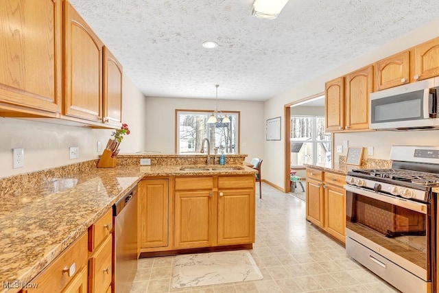 kitchen featuring light stone counters, pendant lighting, stainless steel appliances, a sink, and a textured ceiling