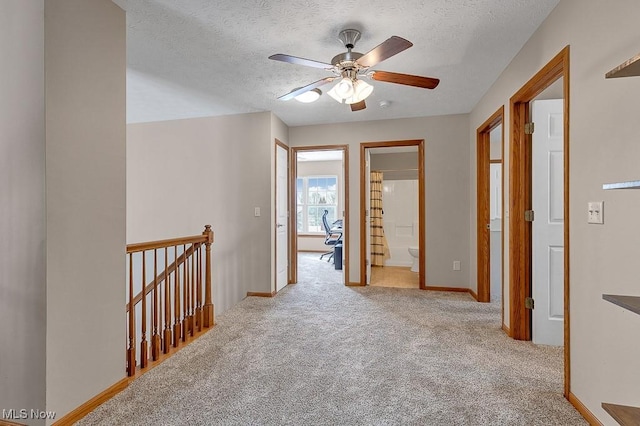 hallway with baseboards, light colored carpet, a textured ceiling, and an upstairs landing