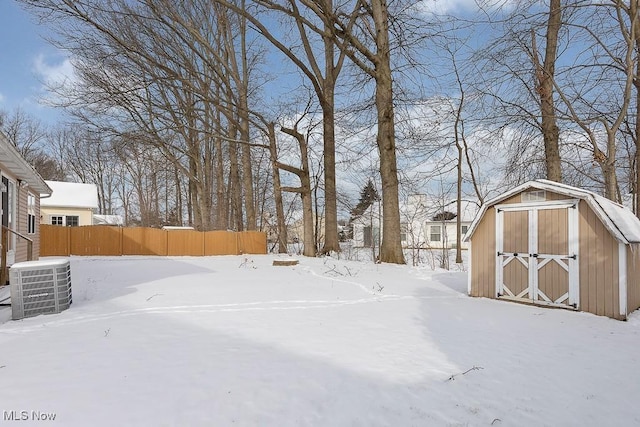 yard layered in snow with an outbuilding, a storage unit, fence, and central air condition unit