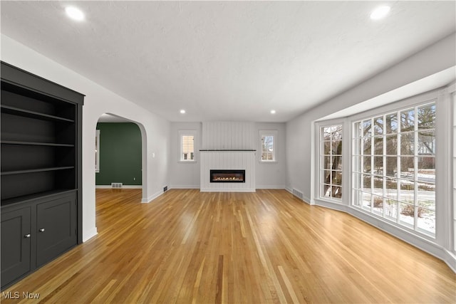 unfurnished living room with a fireplace, a textured ceiling, built in features, and light hardwood / wood-style flooring