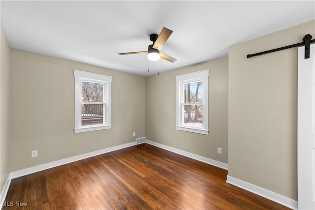 unfurnished room with a barn door, dark hardwood / wood-style floors, and ceiling fan