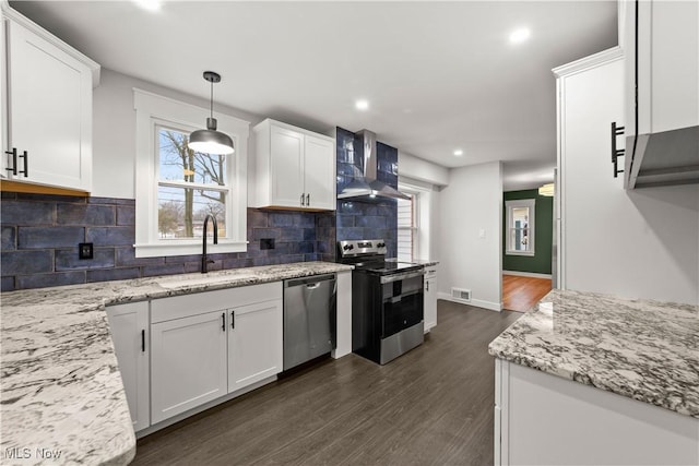 kitchen with appliances with stainless steel finishes, white cabinetry, sink, hanging light fixtures, and wall chimney exhaust hood