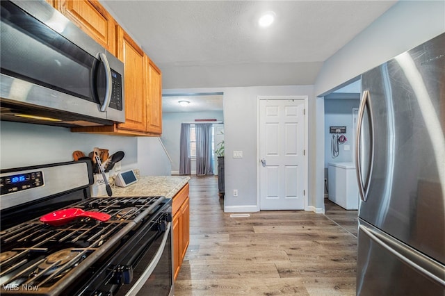 kitchen featuring light stone countertops, stainless steel appliances, and light wood-type flooring