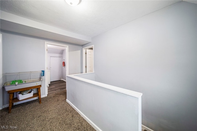 hallway with dark colored carpet and a textured ceiling