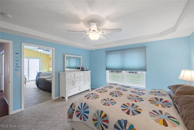 bedroom featuring ceiling fan, a tray ceiling, a textured ceiling, and carpet