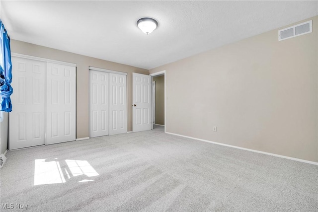 unfurnished bedroom with multiple closets and light carpet