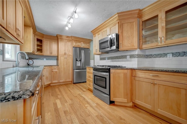 kitchen with appliances with stainless steel finishes, sink, dark stone countertops, and light hardwood / wood-style flooring