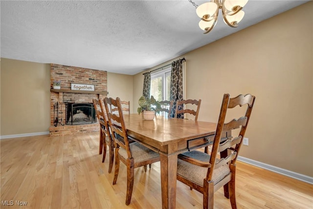 dining area featuring a notable chandelier, a textured ceiling, a fireplace, and light hardwood / wood-style floors