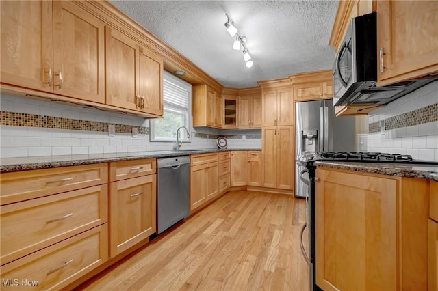 kitchen featuring appliances with stainless steel finishes, a textured ceiling, light hardwood / wood-style flooring, and dark stone countertops