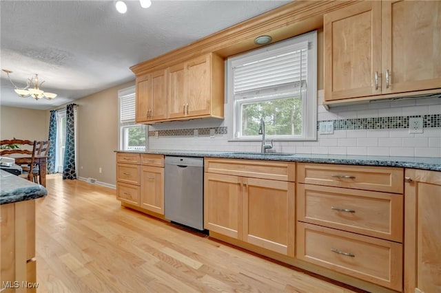 kitchen featuring stainless steel dishwasher, dark stone counters, sink, and light wood-type flooring