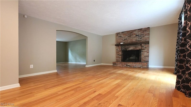 unfurnished living room featuring a brick fireplace, light hardwood / wood-style flooring, and a textured ceiling