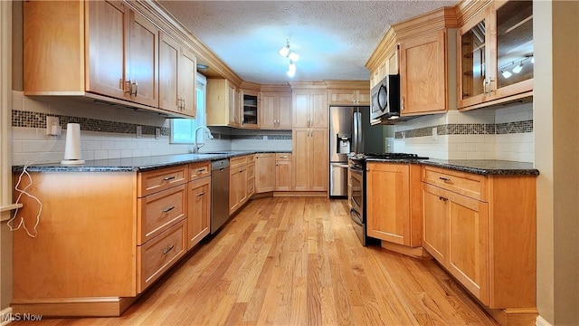 kitchen with sink, a textured ceiling, dark stone counters, light wood-type flooring, and stainless steel appliances