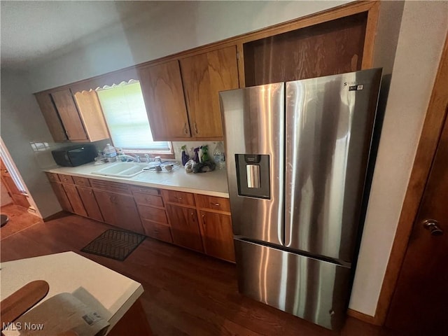 kitchen with brown cabinets, dark wood-style flooring, a sink, stainless steel fridge with ice dispenser, and light countertops