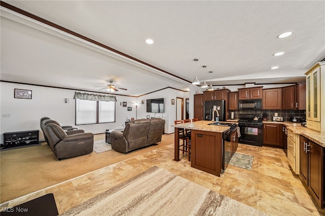 kitchen featuring a breakfast bar, light stone counters, tasteful backsplash, an island with sink, and black appliances