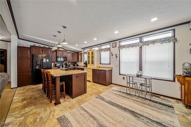 kitchen featuring sink, a breakfast bar area, hanging light fixtures, black appliances, and a center island with sink